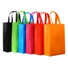 A lineup of colorful reusable non-woven shopping bags in black, green, blue, pink, red, and orange.