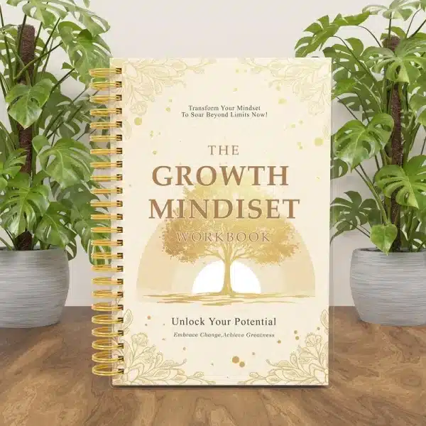 The Growth Mindset Workbook displayed on a wooden desk between two green monstera plants, showcasing its elegant cover.