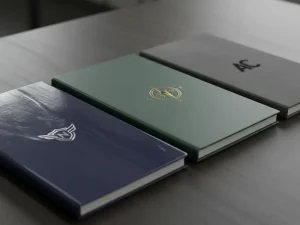 A high-quality close-up photo showing three notebook covers side-by-side one glossy reflecting light, one matte with a smooth finish, and one soft-touch with a velvet texture, showing a professional logo.