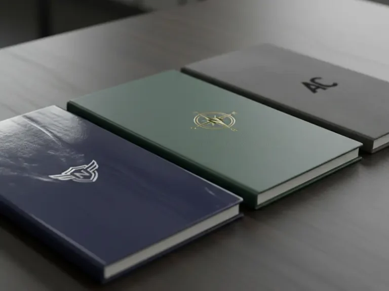 A high-quality close-up photo showing three notebook covers side-by-side one glossy reflecting light, one matte with a smooth finish, and one soft-touch with a velvet texture, showing a professional logo.