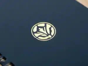 Close-up of a gold foil stamped logo on a dark blue notebook cover with spiral binding
