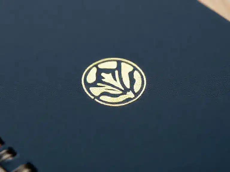 Close-up of a gold foil stamped logo on a dark blue notebook cover with spiral binding