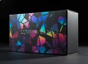 A high-resolution, close-up shot of a premium cosmetic box with a broken glass holographic pattern. The box catches the light, shifting from cyan to magenta. The background is a dark, matte studio setting to e